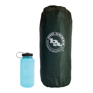 A dark green Big Agnes Tent Stuff Sack 7”x20” stands upright next to a blue water bottle with a black cap, both set against a plain white background.