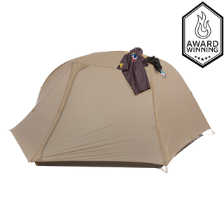 A beige dome-shaped Big Agnes Tiger Wall UL2 Bikepack Solution Dye tent with a jacket on top, shown on a plain white background with an award-winning flame badge in the top right corner.